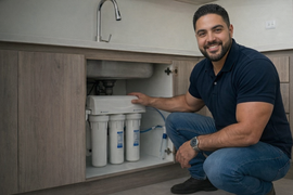 Técnico mostrando sistema de filtración de agua bajo mesón de cocina